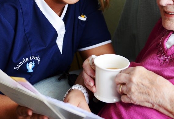 Hands on Care caregiver talking to a resident holding a cup of tea