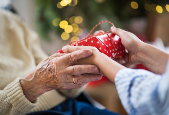 two sets of hands holding a gift in front of a christmas tree