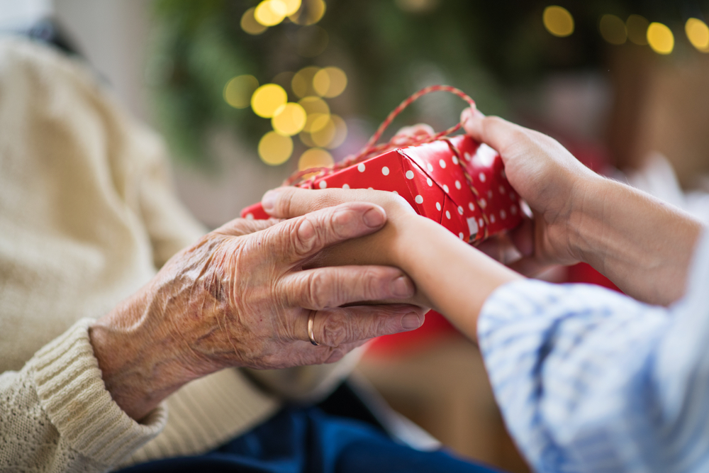 two sets of hands holding a gift in front of a christmas tree