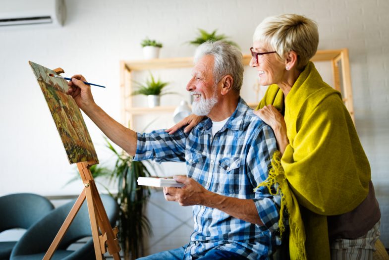 elderly gentlemen painting. Loving partner looking on.