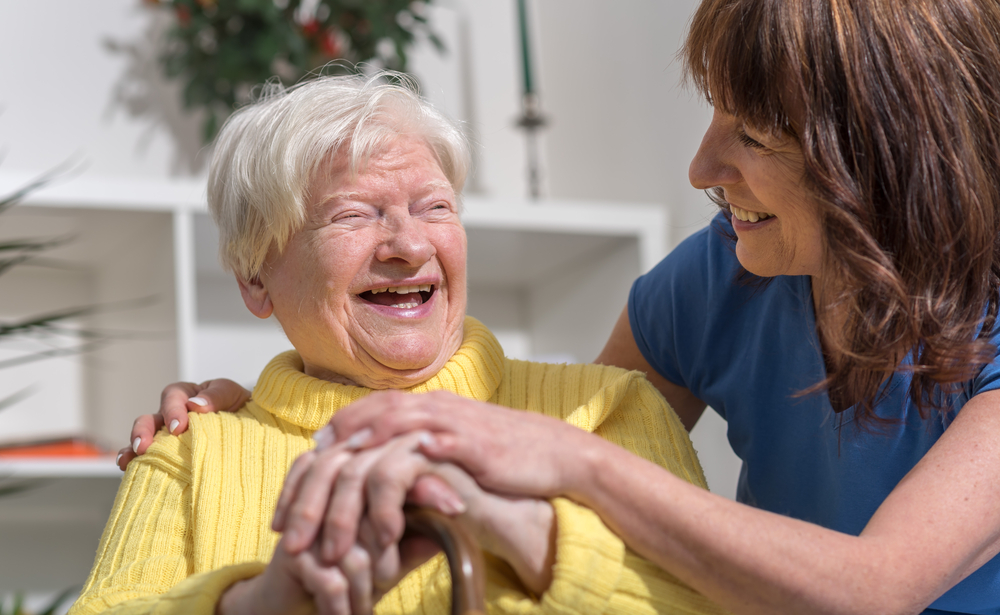 An elderly person smiling and laughing with a caregiver.