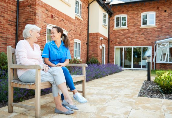 Resident and a caregiver sitting on a bench outside of an assisted living facility.