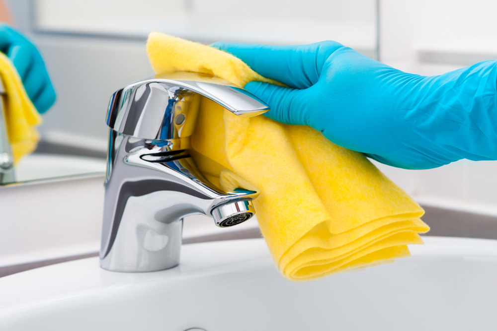 Hands On Care cleaner sanitising and polishing a bathroom tap during a professional cleaning service.